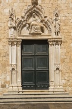 Ornate dark green entrance door decorated with carved religious figures at Franciscan Monastery,