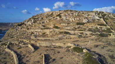 Drone image, Archaeological excavation site, A rocky hill under blue sky with visible dry stone