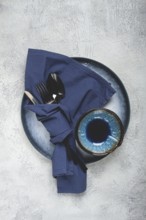 Food background, with an empty blue plate, a bowl, black cutlery, with a napkin, on a gray