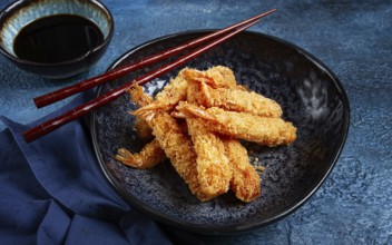 Shrimp in tempura, deep fried, on a black plate, with soy sauce, close-up, top view, no people