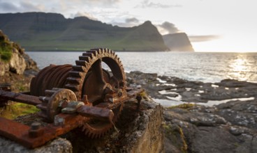 Iron winch with large cogwheel, designed to pull boats ashore, sea with mountains and low sun,