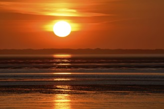 Sunset over the North Sea at low tide, the outline of the island of Juist on the horizon,