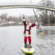 Water sports enthusiasts dressed as Santas ride SUPs on the Spree in front of the Insel der Jugend