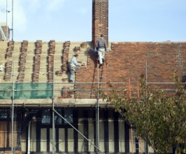 Men re-roofing historic building with clay tiles, Thorpeness, Suffolk, England, United Kingdom,