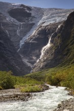 The melting glacier Kjenndalsbreen feeds a waterfall that flows into a wild river, surrounded by