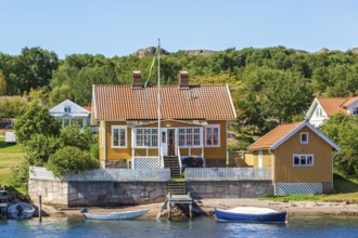 Idyllic summer cottage by a sea beach with a jetty and boats in the Swedish archipelago in the