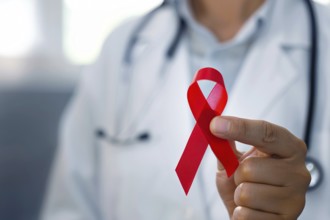 Red AIDS awareness ribbon held by doctor's hand. Generative AI, AI generated