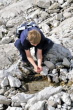 Ten-year-old boy hiking, refreshing himself at a spring, Nebelhorn, Allgäu Alps, Bavaria, Germany,