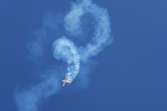 Stunt aerobatic plane performing stunts rolls loops in blue sky with smoke trail. Concept of speed,