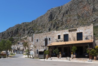 A Mediterranean village with stone buildings in front of a rocky mountain landscape under a clear