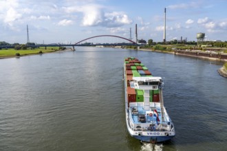 The Dutch cargo ship Vrido, loaded with containers, on the Rhine near Duisburg, descending, behind