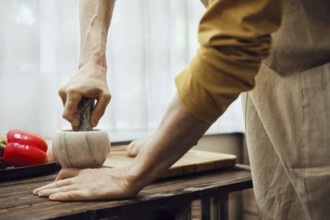 Unrecognizable man grinds pepper in a mortar using a pestle