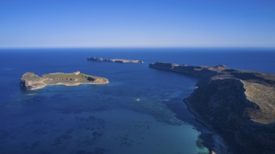 Drone shot, panoramic view of two islands, one with green vegetation and one rocky, surrounded by