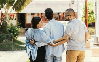 Unfaithful girl walking in the park with her boyfriend while holding another man hand. Woman