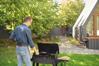 Middle-aged man puts a griddle pan with steak on barbecue grill while making food at backyard