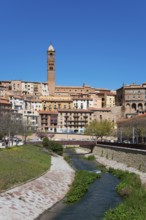 Historic town with a stone tower, river in the foreground and several shops and residential