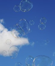 Soap bubbles float in front of a clear blue sky with a small white cloud, Spain, Europe