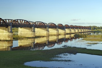 Long, arched stone bridge reflected in the calm river water under a clear sky, autumn, Elbe,