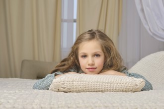 Young girl enjoys a moment of relaxation, lying face down on a comfortable bed with soft pillows in