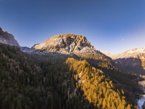 Sunrise illuminates the snow-covered peak and autumnal forest, Bad Reichenhall, Bavaria, Germany,