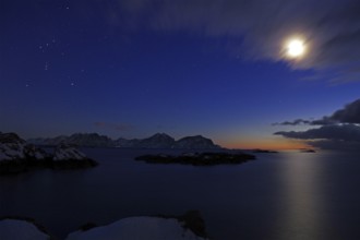 Dark coastal landscape at dusk with snow-covered islands, moon, stars and few clouds, winter,