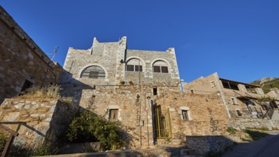 A medieval stone castle built on a hill, under a clear blue sky, Vathia, residential tower village,