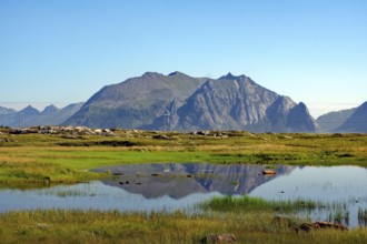 A peaceful natural landscape with a mountain and a lake reflecting the surrounding rocks and sky,