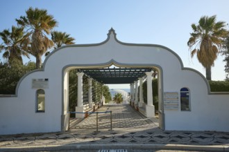 Decorative entrance gate in a white building, surrounded by palm trees, overlooking a sunny sea,