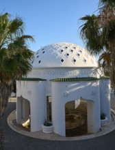 White, decorative domed architecture surrounded by palm trees under a clear sky, thermal springs,