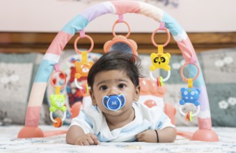 Baby boy playing lying on bed with pacifier on mouth