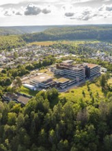 Large building surrounded by a green forest and town, seen from the air under a cloudy sky,