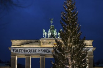 A banner For Democracy in Syria / Defend Rojava hangs behind a Christmas tree at the Brandenburg