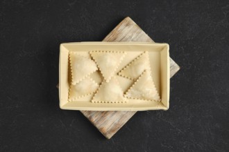 Freshly made ravioli are arranged neatly in a rectangular tray on a rustic wooden board. Each pasta