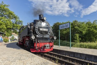 A steam locomotive stands at the railway station with a sign in summer weather, Rügen, Rasender