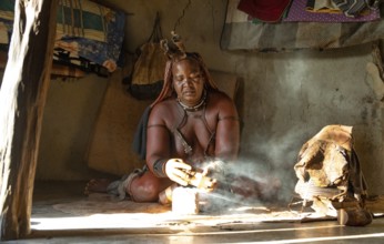 Traditional Himba woman prepares herbs for body care with smoke, Interior of the first woman's mud