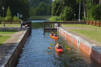 Two canoeists on a water canal under a small bridge in a wooded area, Sluza Perkuc, Perkuc lock,