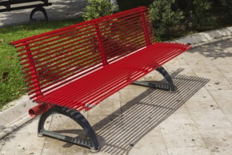 Red painted sitting bench with seat and backrest made of round metal tubes on the grounds of the