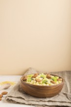 Millet porridge with kiwi and almonds in wooden bowl on a white and orange background and linen