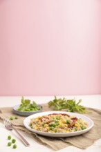 Quinoa porridge with green pea, corn and dried tomatoes on ceramic plate on a white and pastel pink