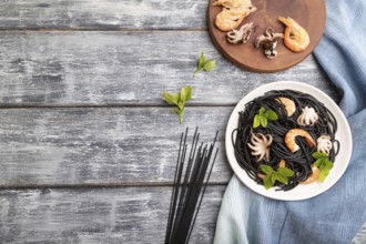 Black cuttlefish ink pasta with shrimps or prawns and small octopuses on gray wooden background and