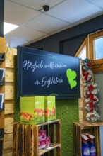 Welcome sign in a shop with green decoration and wooden shelves, Tante M, self-service shop,