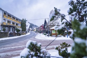 Snowy road through a wintry village with trees and traditional houses, Enzklösterle, district of