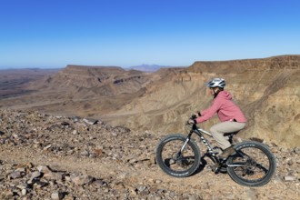 Woman riding a mountain bike, fatbike, on the edge of the abyss, behind the gorge landscape of the