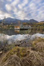 Boathouses in the lake at sunrise, Lake Kochel in autumn with reflection, behind mountain peaks