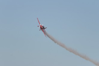 Red stunt aerobatic plane performing stunts in blue sky. Concept of speed, difficulty, precision,