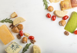 Set of different types of cheese with rosemary and tomatoes on a white wooden background. Top view,