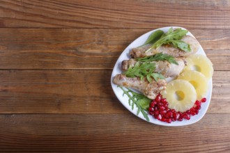 Fried chicken legs with rucola, pineapple and pomegranate seeds on brown wooden background, copy