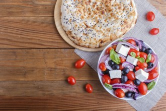 Greek salad with fresh cherry tomatoes, feta cheese, black olives, basil and onion on wooden