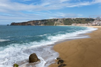 View of the beach coast of Nazaré with waves, sand and a picturesque hill in the background, Praia