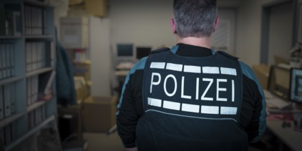 A police officer in uniform stands in an office with screens and files, symbolic image search,